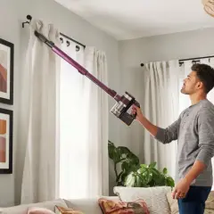 Uomo aspira le tende con un aspirapolvere senza fili. Un modo semplice per capire come pulire le tende da sole.