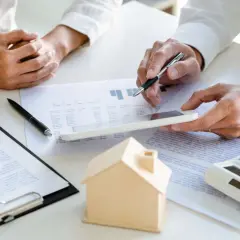Manos revisando documentos y una casa de juguete, discutiendo qué cubre el seguro de hogar.