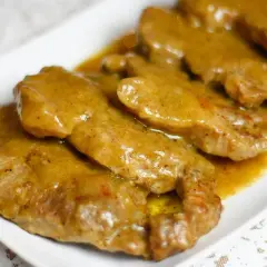 Karkówka w sosie, podana na białym talerzu. Mięso jest delikatne i pokryte gęstym, aromatycznym sosem.
