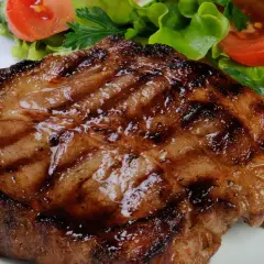Bistecca di maiale succulenta e grigliata, servita con un'insalata fresca di lattuga, pomodoro e cetriolo.