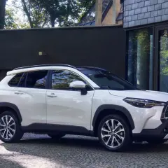 Biała Toyota Corolla Cross zaparkowana przed nowoczesnym budynkiem. Sprawdź jej wymiary, by poznać jej kompaktową sylwetkę.