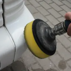 Dłoń trzyma polerkę z żółtą gąbką, polerując biały lakier samochodu.
