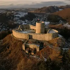 Zamek Rytro, kamienne ruiny na wzgórzu, otoczone zimowym krajobrazem i miasteczkiem.
