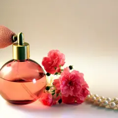 Frasco de perfume rosa con atomizador, rosas rosadas y collar de perlas. Un aroma que evoca la dulzura del almizcle que es.