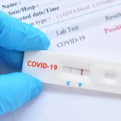 Ręka w niebieskiej rękawiczce trzyma test antygenowy COVID-19 z dwoma widocznymi paskami, wskazującymi na wynik pozytywny.
