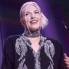 Daria Zawiałow w błyszczącej kreacji, z błyszczącymi ozdobami na twarzy, uśmiecha się na scenie.
