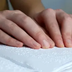 Dłonie osoby czytającej książkę w alfabecie Braille'a.