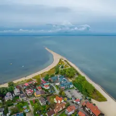 Widok z lotu ptaka na malowniczą miejscowość nad morzem, z domkami i plażą wcinającą się w spokojne wody. Idealne miejsce na wakacje.