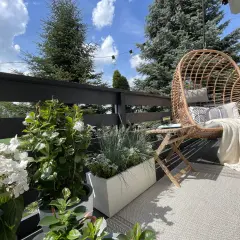 Przytulny mini balkon w bloku z fotelem wiszącym, stolikiem i kwitnącymi roślinami. Idealne miejsce na relaks.