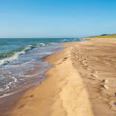 Spokojne, dzikie plaże nad Bałtykiem. Fale delikatnie obmywają piaszczysty brzeg, a na piasku widać ślady stóp.