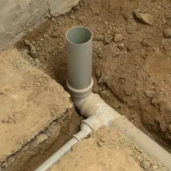 Instalacja kanalizacyjna w domu w trakcie budowy. Szare rury PVC połączone w wykopie ziemnym.