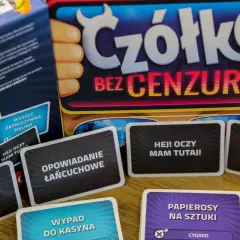 Karty z gry "Czółko Bez Cenzury" leżą na stole. Widać hasła takie jak "Opowiadanie na małpę" i "Hej! Oczy mam tutaj!".
