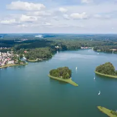 Malownicze jeziora w Polsce z wyspami porośniętymi drzewami i żaglówkami na wodzie. W oddali widać lasy i zabudowania.
