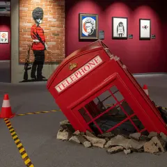 Wystawa Banksy Warszawa: przewrócona budka telefoniczna, mural z żołnierzem i prace artysty.