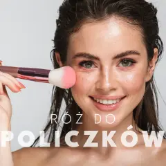 Uśmiechnięta kobieta nakłada róż do policzków pędzlem. Dowiedz się, jak dobrać róż, by uzyskać naturalny efekt.
