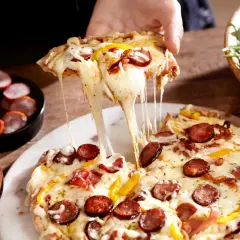 Rozciągający się ser z kawałka farmerskiej pizzy z kiełbasą i papryką. Obok miseczka z rukolą i wędlinami.