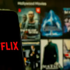 Telefon z logo Netflix na tle ekranu z filmami. Zastanawiasz się, co obejrzeć na Netflixie?