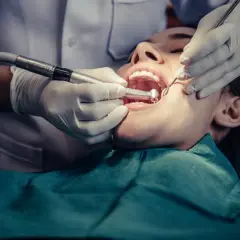 Dentista trabajando en la boca de una paciente, realizando una **conclusión dental** con instrumental y pieza de mano.