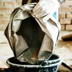 Rękawica zrzuca cement z worka do wiadra, przygotowując mieszankę. Kluczowe są odpowiednie jak zrobić beton proporcje.