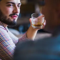 Mężczyzna z zarostem, w kratę, trzymający szklankę z bursztynowym płynem. W jego oczach widać pustkę, typową dla narcyza alkoholika.