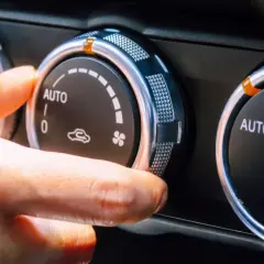 Dłoń reguluje pokrętło klimatyzacji w samochodzie, ustawiając tryb AUTO. Włączony jest czynnik chłodniczy, zapewniając komfortową temperaturę.