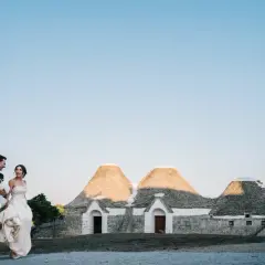 Sposi passeggiano sorridenti davanti a trulli, un'immagine perfetta per le canzoni ingresso sposi.