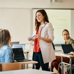 Nauczycielka wyjaśnia studentom, jak zostać nauczycielem po innych studiach. Uczniowie pracują na laptopach w sali lekcyjnej.