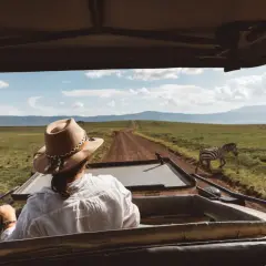 Mujer con sombrero en un safari en Tanzania, observando cebras en la sabana.