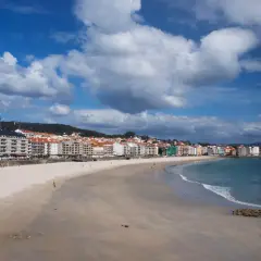 Amplia playa de Silgar con edificios residenciales al fondo y el mar azul bajo un cielo nublado.