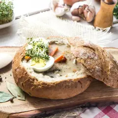 Pyszny żurek wegetariański w chlebie, udekorowany jajkiem i kiełkami. Obok przyprawy i jajka przepiórcze.