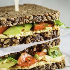 Delicioso sandwich de hummus con aguacate, tomate y pan integral con semillas.