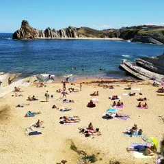 Gente disfrutando del sol y el mar en la playa de cerrias, con formaciones rocosas impresionantes.