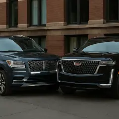 Dwa luksusowe SUV-y, granatowy Lincoln Navigator i czarny Cadillac Escalade, stoją obok siebie na tle ceglanego budynku.