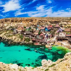 Bunte Häuser am malta beach, umgeben von Felsen und türkisfarbenem Wasser. Boote schaukeln sanft in der Bucht.