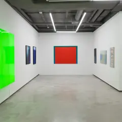 Galeria sztuki z neonowo-zieloną instalacją i obrazami, w tym dziełem Stefana Gierowskiego.
