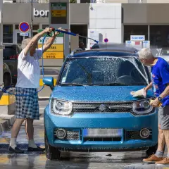 Deux hommes lavent une machine bleue avec de la mousse. L'un utilise un nettoyeur haute pression, l'autre frotte avec une éponge.