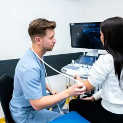 Lekarz wykonuje usg narządu ruchu u pacjentki, badając jej ramię. Na ekranie widoczny obraz ultrasonograficzny.
