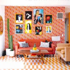 Vibrant living room with a bold 70s aesthetic. Orange patterned wallpaper, a cactus, and colorful art create a retro vibe.