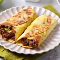 Dwie tortille z mięsem mielonym i serem, podane na talerzu z zieloną serwetką. Pyszne danie gotowe do jedzenia.