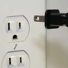 Zalane gniazdko elektryczne. Czarny wtyk zbliża się do białej obudowy, grożąc zwarciem.