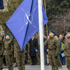 Uroczystość z flagą Organizacji Traktatu Północnoatlantyckiego. Żołnierze w mundurach oddają honory.