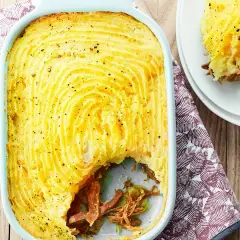 Un parmentier de canard doré et gratiné, prêt à être dégusté. Une portion est servie sur une assiette blanche.