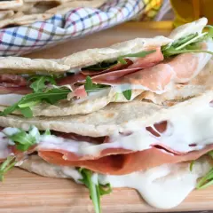 Piadina farcita con prosciutto crudo, mozzarella filante e rucola. Una ricetta piadina veloce e gustosa, perfetta per un pranzo o una cena informale.