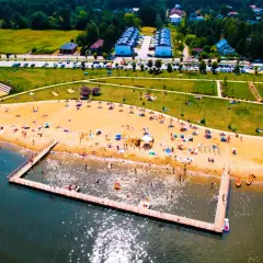 Słoneczny dzień nad zalewem żyrardowskim. Ludzie odpoczywają na plaży, kąpią się w wodzie i spacerują po molo.