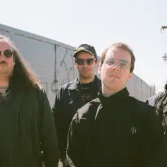 Czterech mężczyzn, jakby z zespołu The Sisters of Mercy, pozuje na tle wagonów kolejowych.