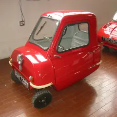 Czerwony, trójkołowy samochód Peel P50, najmniejszy pojazd na świecie, stoi na ceglanej podłodze.