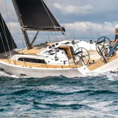 Un uomo guida una barca a vela bianca con vele nere, solcando le onde. Il nome "Xelebration" è visibile sullo scafo.