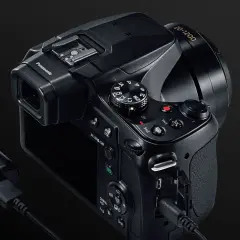 Czarny aparat Panasonic Lumix FZ82 z obiektywem 20-1200, podłączony do ładowarki.