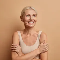 Glad kvinna med blont hår ler och tittar uppåt, funderar på hur mycket kollagen per dag som är bäst för huden.