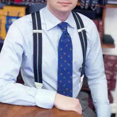 Elegancki mężczyzna w błękitnej koszuli, ozdobionej wzorem z ptakami, ma na sobie stylowe szelki i krawat.